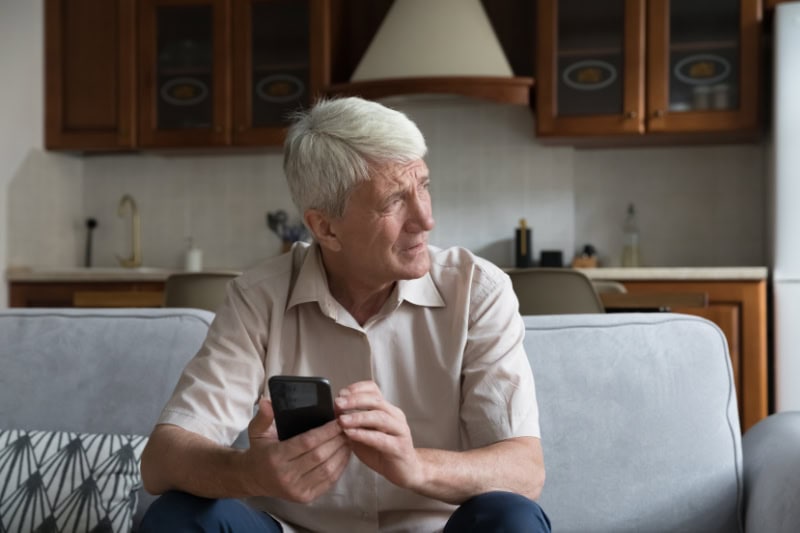 What’s That Smell Coming From My Furnace? Photo of a man sitting on his couch with his phone in his hand, looking out a window seemingly concerned.